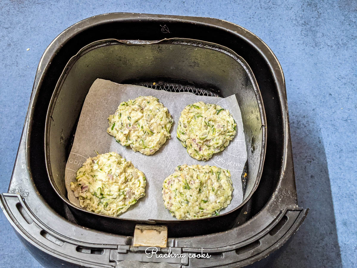 Air fryer with parchment paper cut to size with zucchini fritters on top
