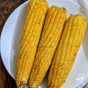 3 air fried corn on the cob on a white plate.