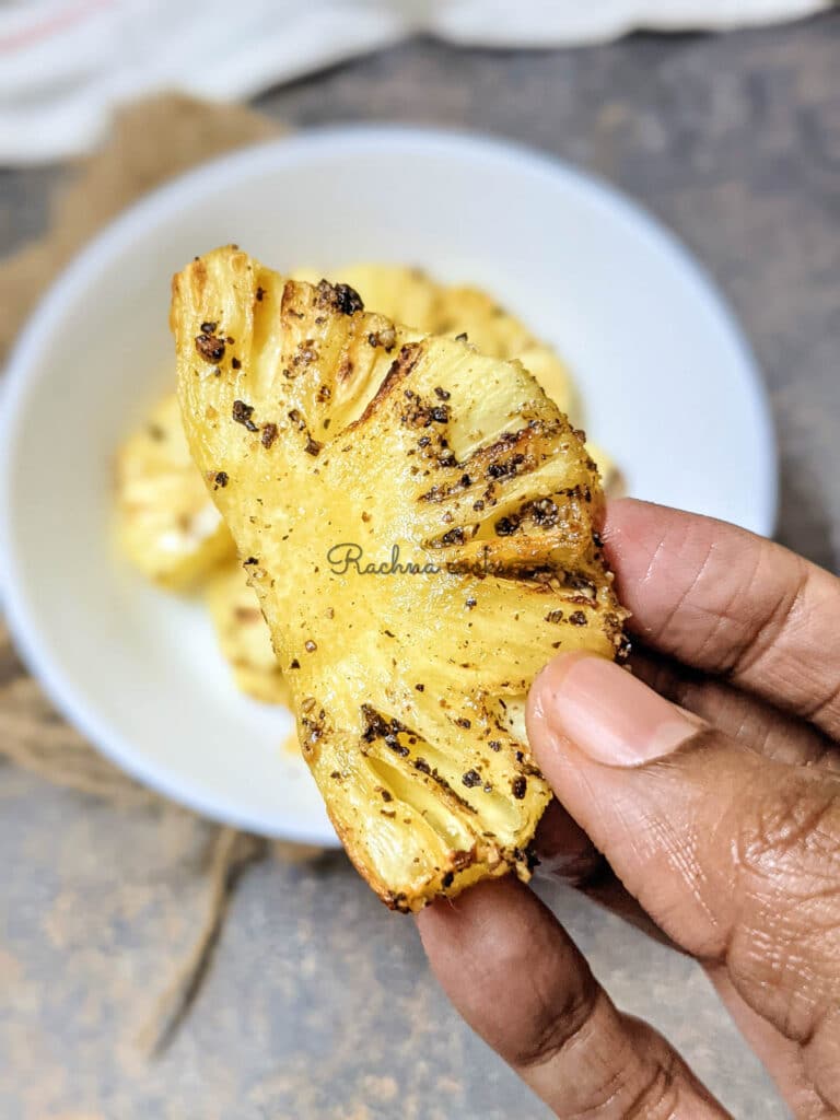 Close up of a roasted pineapple slice held up in hand