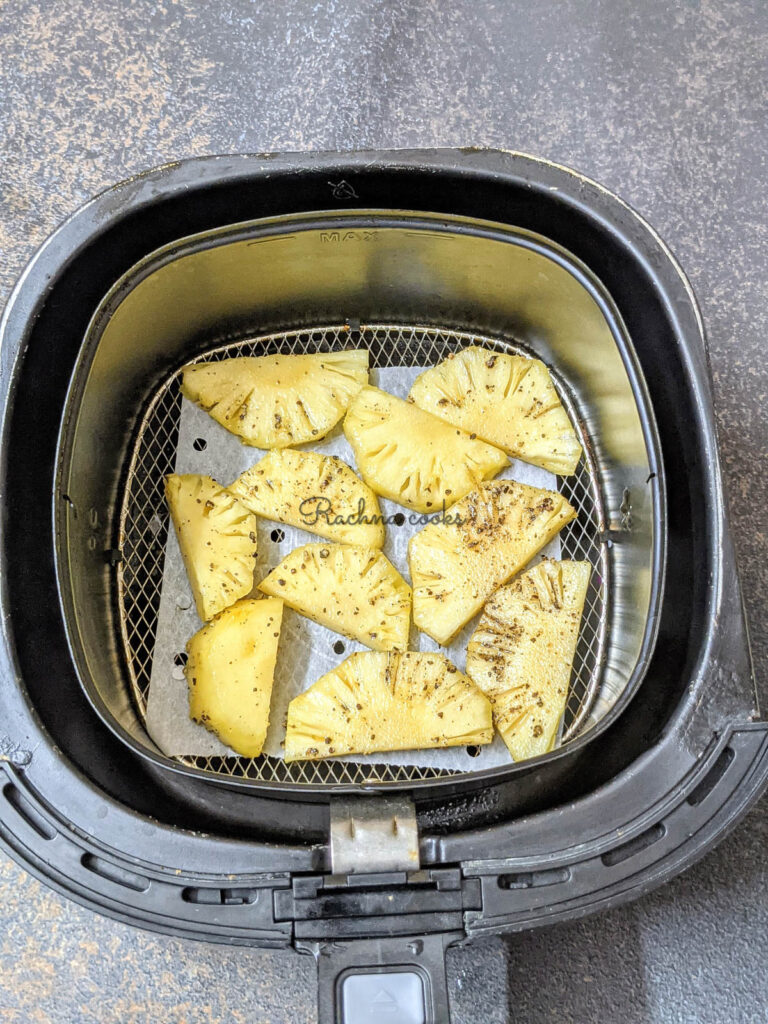 Marinated pineapple slices on a perforated parchment paper in air fryer basket.