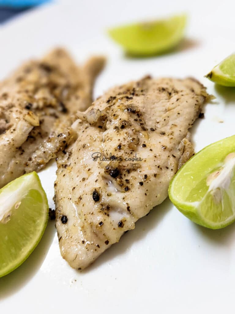 Air fryer tilapia fillet in closeup with lemon wedges on a white plate