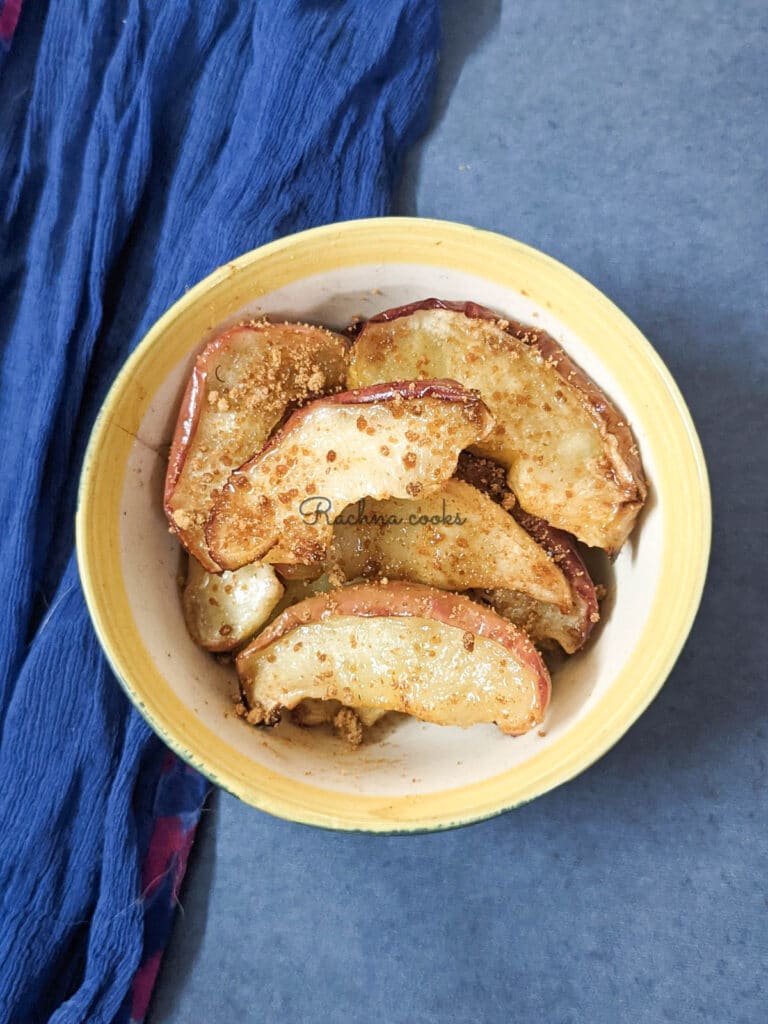 Air fried apple slices in a blue bowl with a blue background with a sprinkling of brown sugar visible.