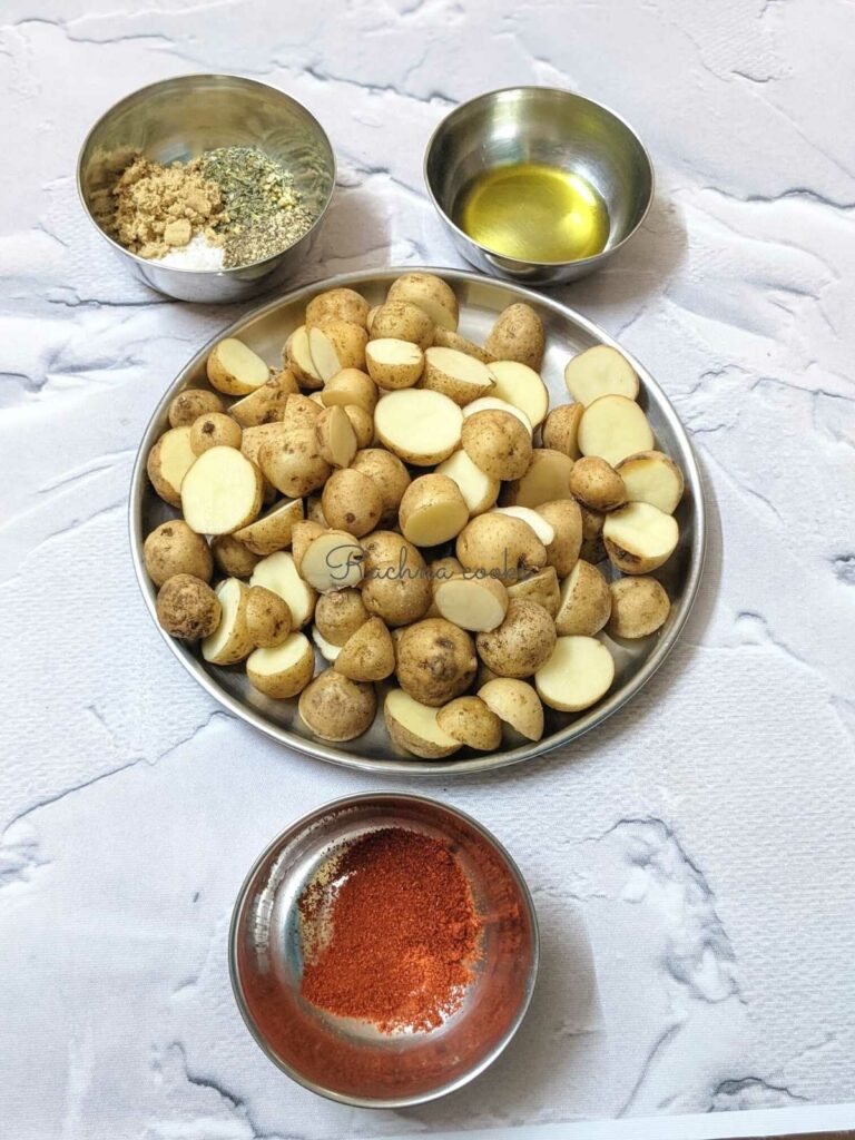 Baby potatoes cut in halves in a plate, with bowls of olive oil, spices and paprika.
