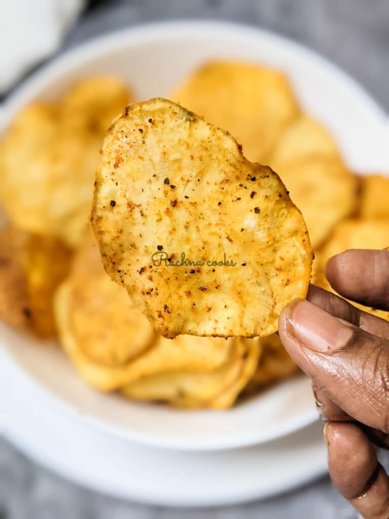 One crispy air fried sweet potato chip in focus with other blurred chips in the background.