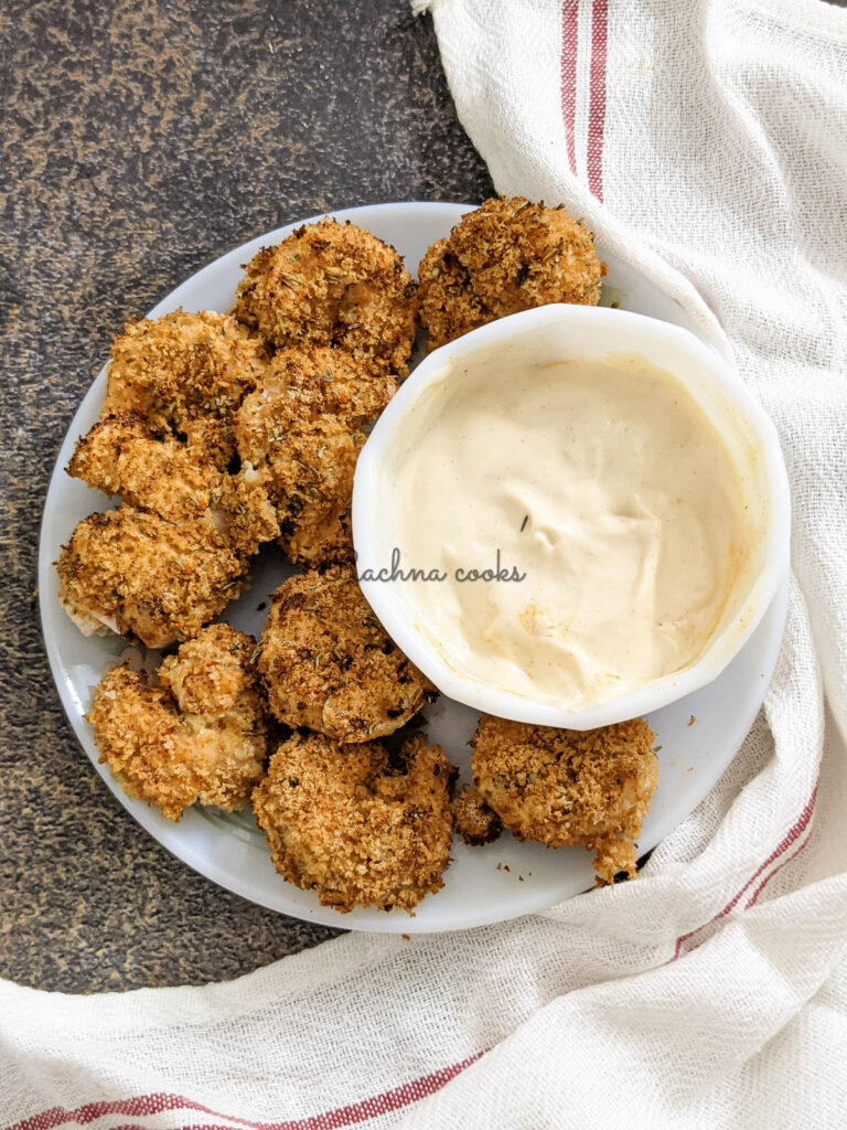 Crunchy air fried shrimp with a bowl of cream bang bang sauce in a white bowl. This is on a brown background with a white napkin visible.