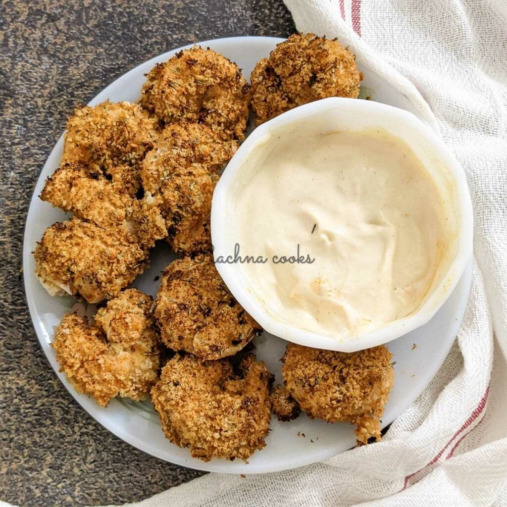 Crunchy air fried shrimp with a bowl of cream bang bang sauce in a white bowl. This is on a brown background with a white napkin visible.