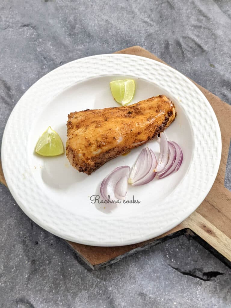 Air fried mahi mahi fillet that looks golden brown on a white plate with sliced onion and lemon cut into pieces.