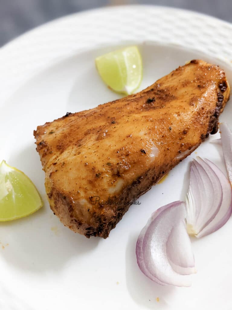 Air fried mahi mahi fillet that looks golden brown on a white plate with sliced onion and lemon cut into pieces.