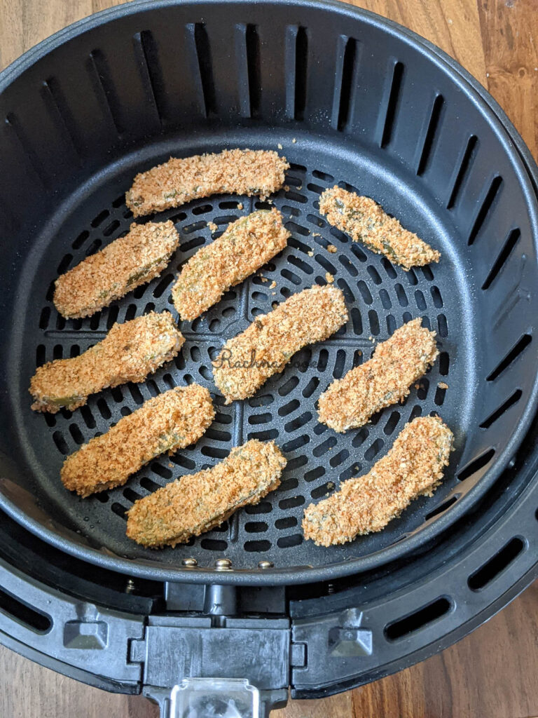 Air fryer basket laid with breaded pickle slices.