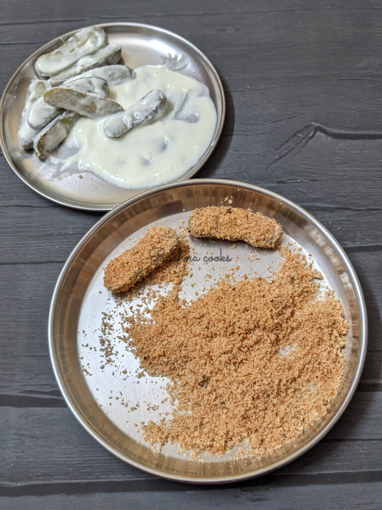 Some pickle slices dredged in yogurt slurry  in a shallow plate and 2 pickle slices dredged in breadcrumbs in another shallow plate.