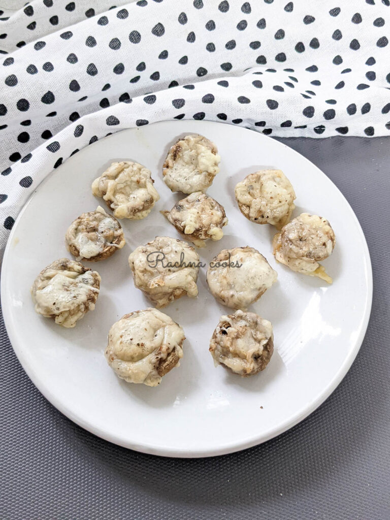 Stuffed mushrooms with cheese all around them on a white plate on a grey background.