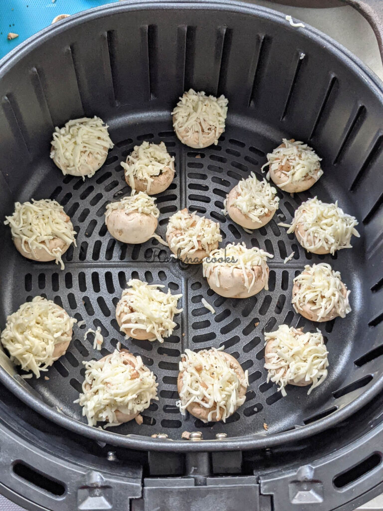 Mushroom caps stuffed and garnished with grated cheese ready for air frying in air fryer basket.