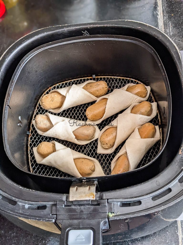 Wrapped pigs in a blanket in air fryer basket ready for air frying.