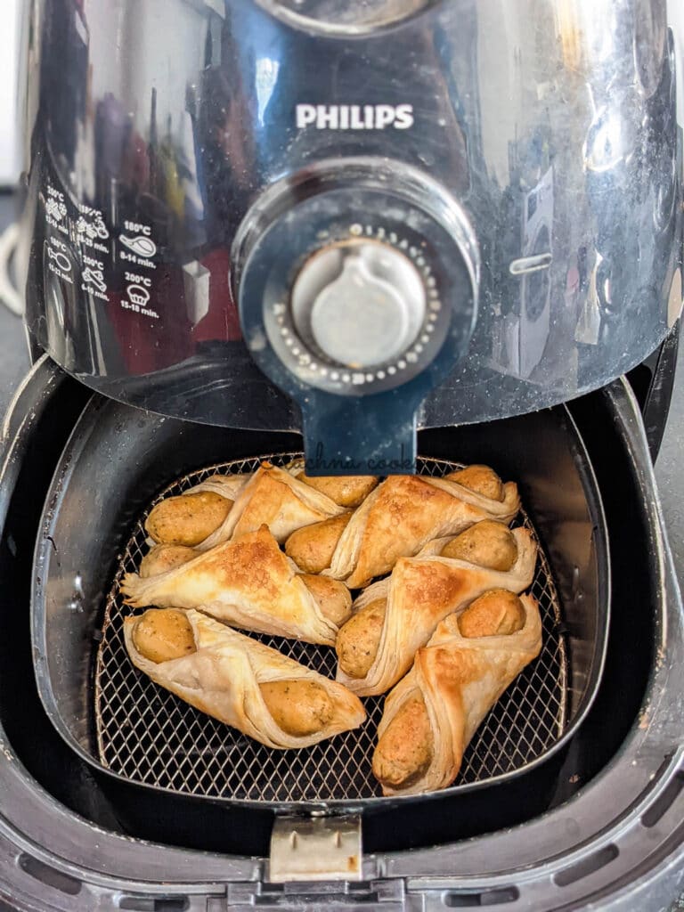 Golden brown and air fried close up of six pigs in a blanket in air fryer basket 