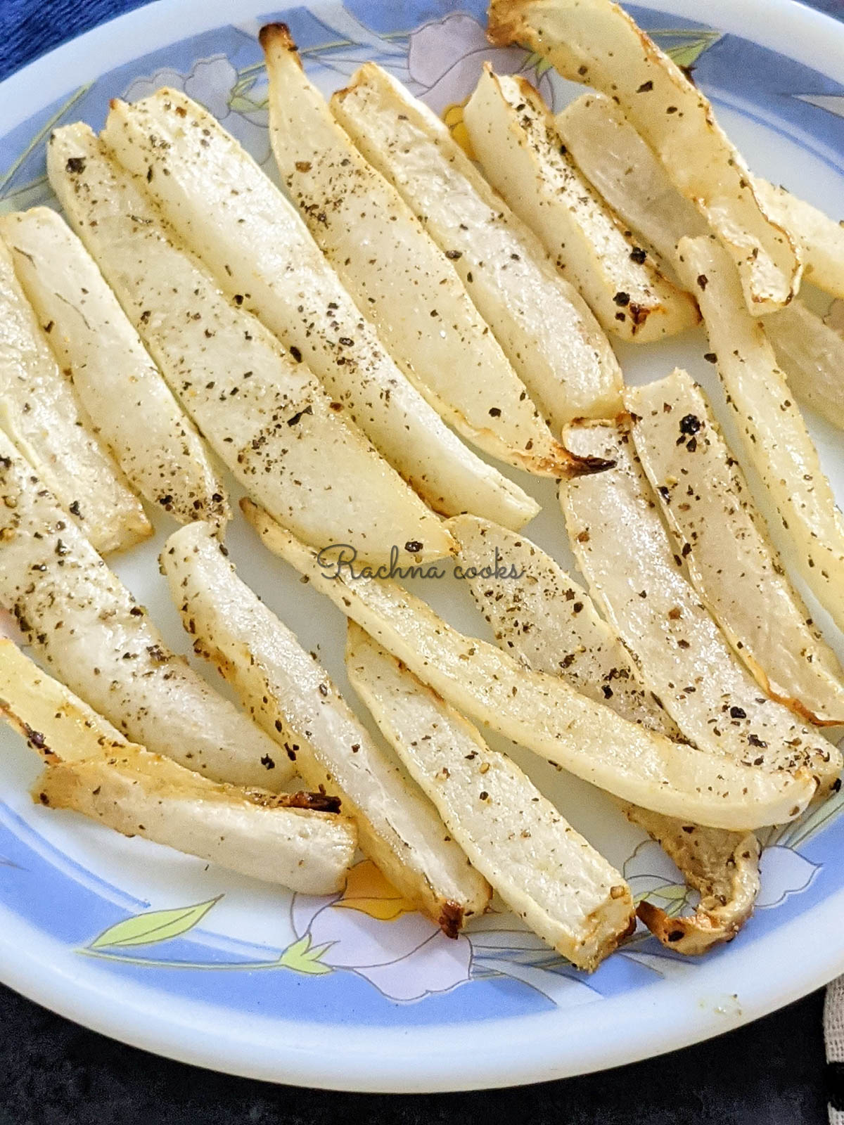 A close up of air fried parsnip fries in a white plate with blue design on the edges.