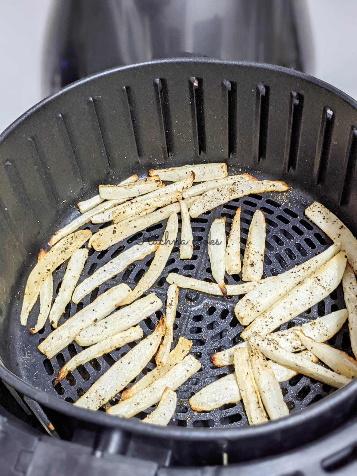 Air fried parsnip snips with golden brown edges in air fryer basket after air frying.
