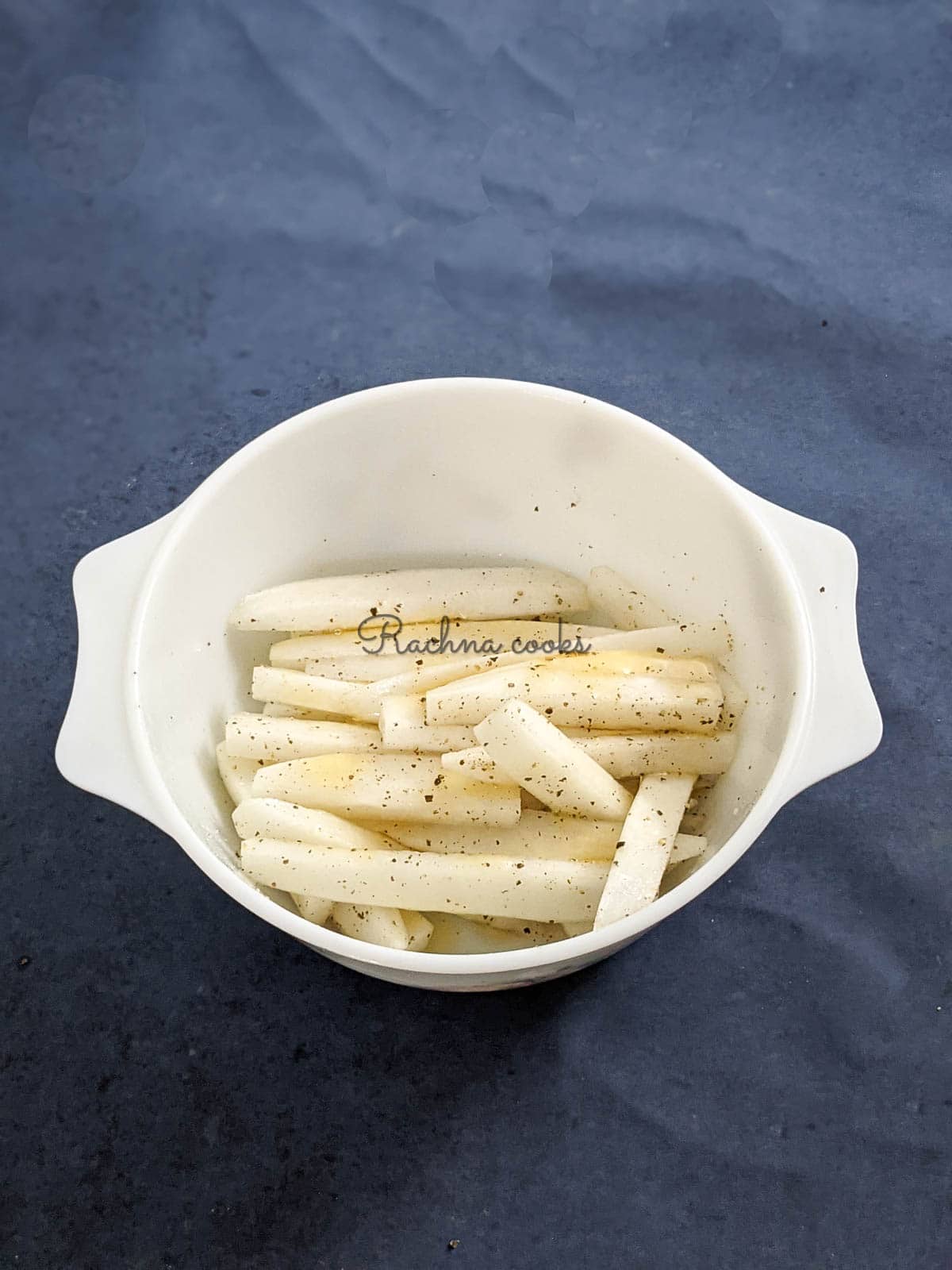 Parsnip fries in a white bowl with salt, pepper, honey/maple syrup and olive oil tossed in.
