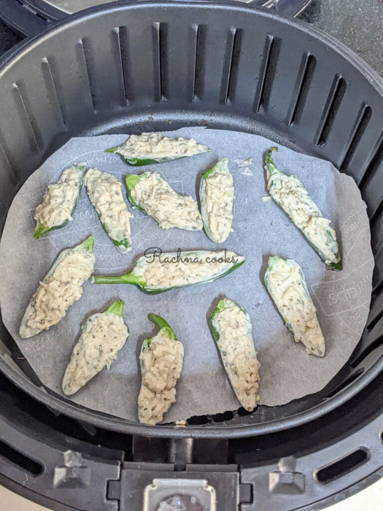 Jalapeno poppers with stuffing lined on parchment lined air fryer basket.