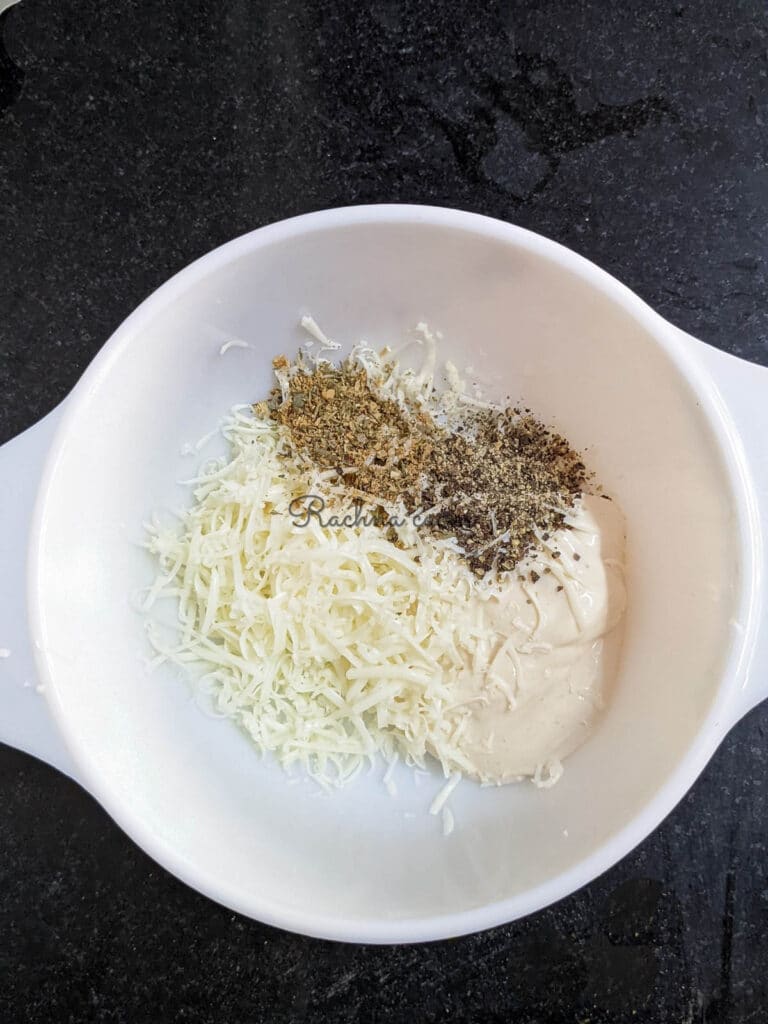 A white bowl with cream cheese, grated cheese, pepper, garlic powder, Italian seasoning and salt