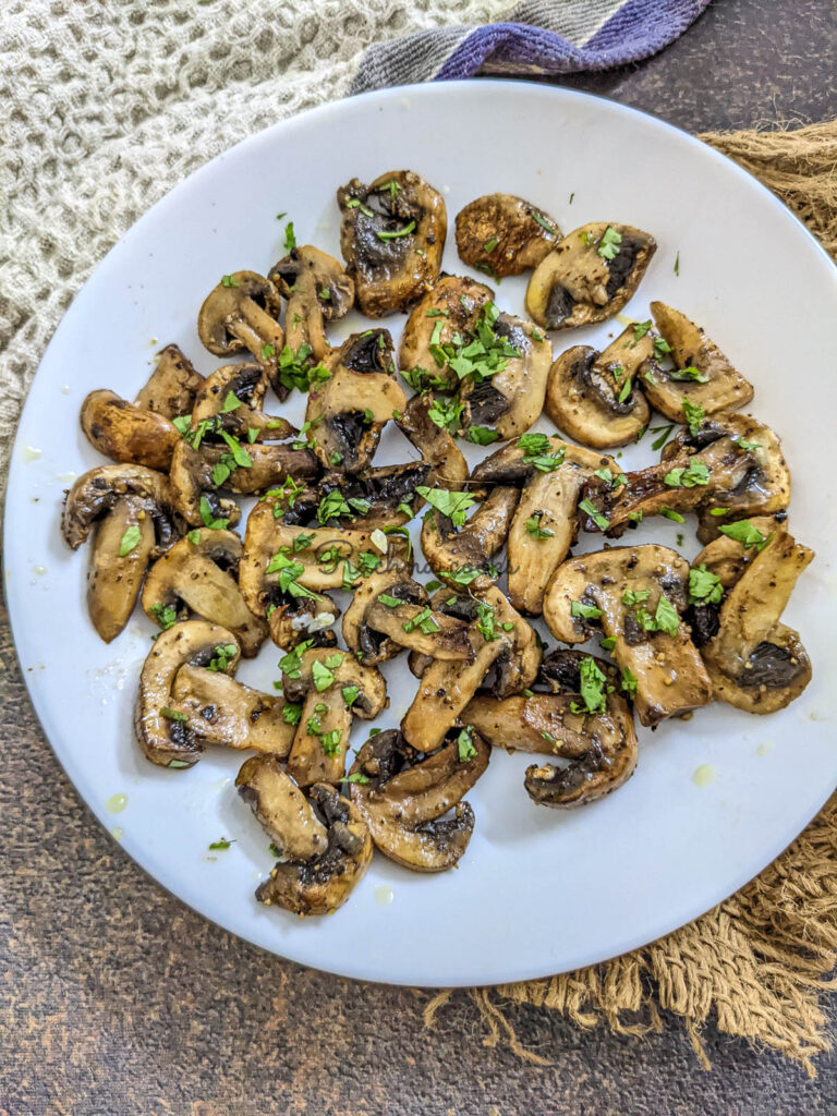 Crispy juicy air fried mushroom slices garnished with cilantro leaves on a white plate.