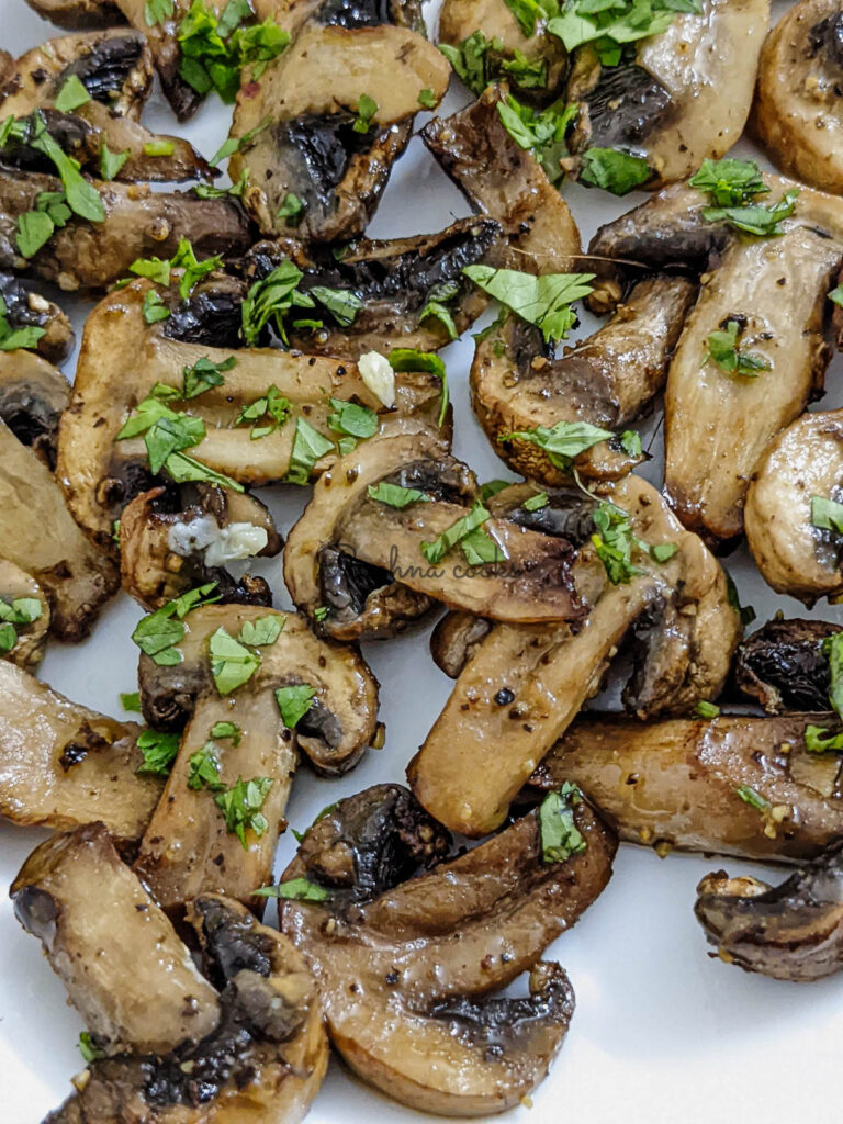 Close up of crispy juicy air fried mushroom slices garnished with cilantro leaves on a white plate.