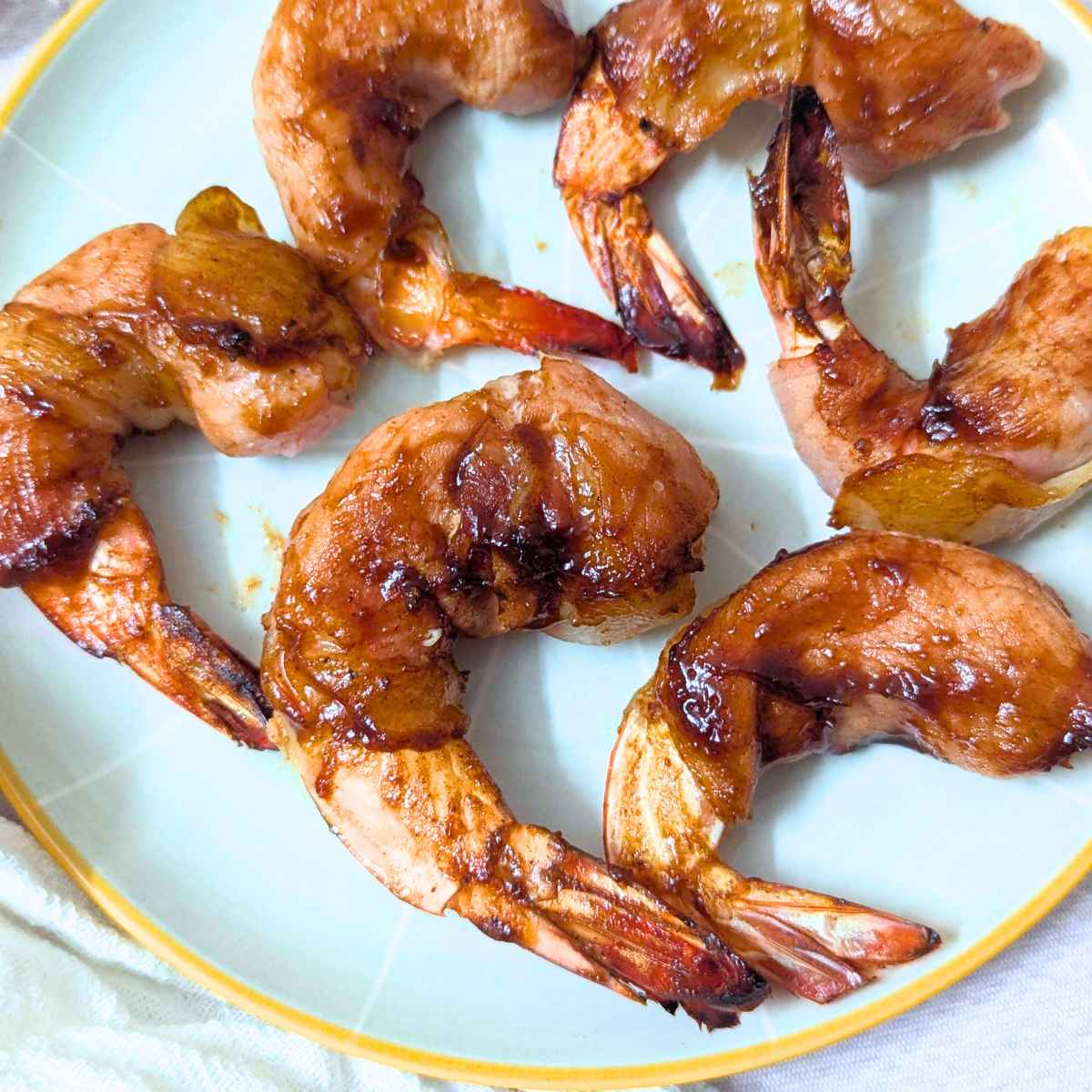 Bacon wrapped shrimp after air frying on a plate.