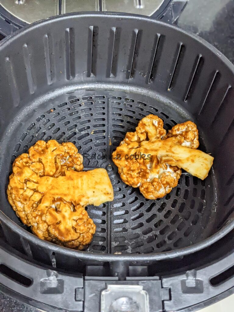 Two cauliflower steaks in air fryer basket ready for air frying.