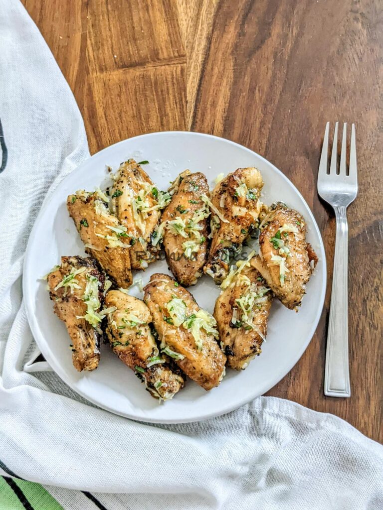 Delicious air fried garlic parmesan wings on a white plate with grated parmesan and parsley on top.