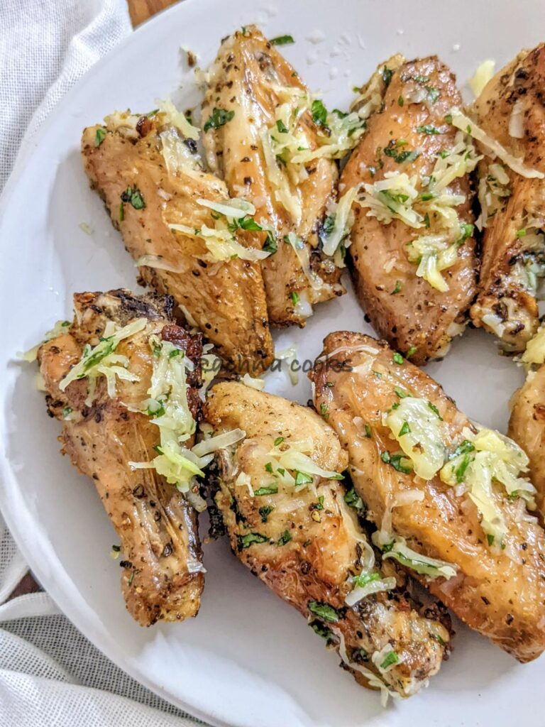 Delicious air fried garlic parmesan wings on a white plate with grated parmesan and parsley on top.