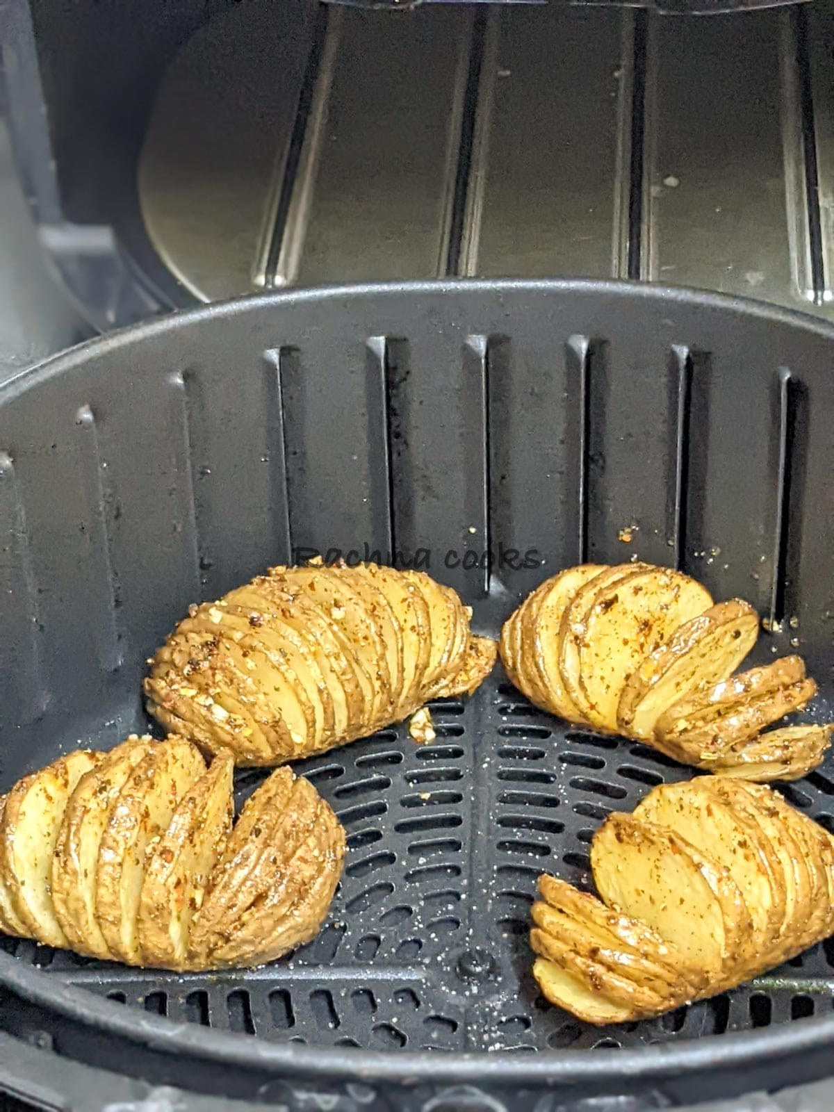 four Hasselback potatoes golden and beautifully cooked after air frying in air fryer basket.