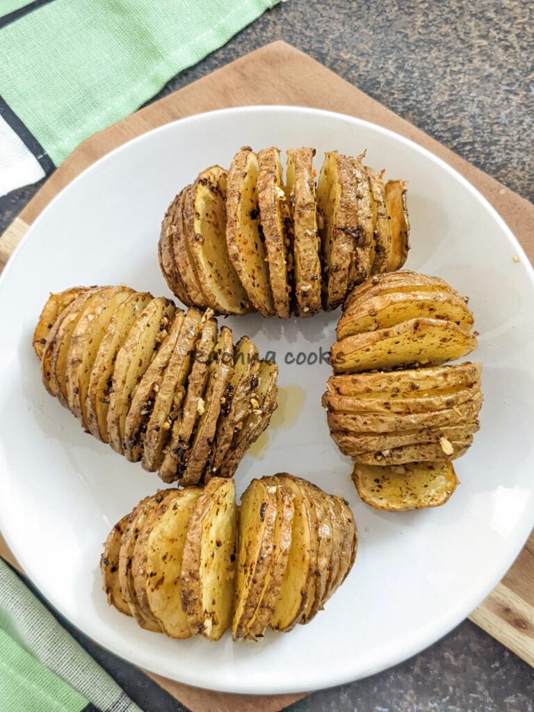top shot of Four hasselback potatoes after air frying on a white plate with a green napkin on a brownish background.