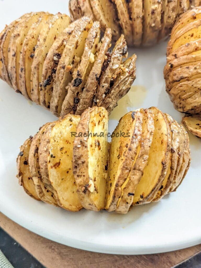 Close up of two hasselback potatoes with four of them after air frying on a white plate.