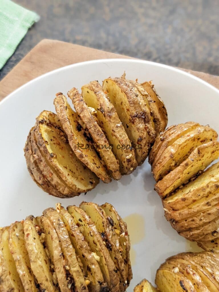 Close up of four hasselback potatoes after air frying on a white plate 