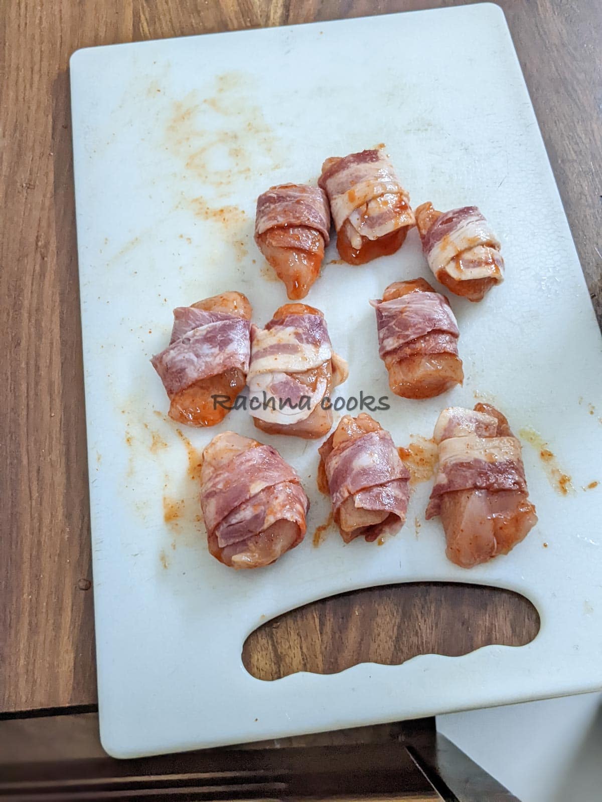 Chicken bites brushed with Sriracha sauce and wrapped with bacon strips on a chopping board.