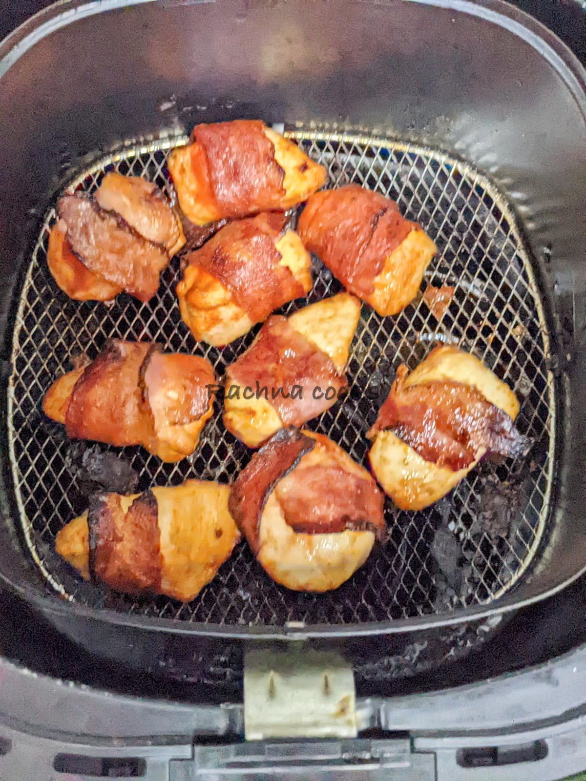 Browned bacon enwrapping cooked chicken bites in air fryer basket ready to be eaten.