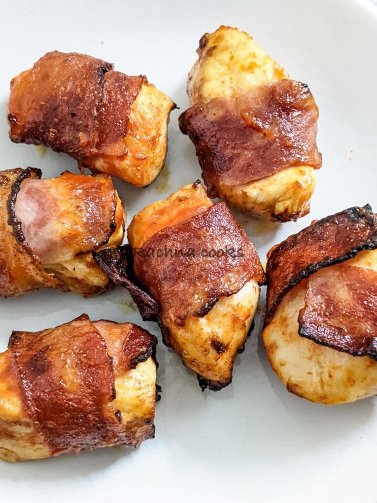 Close up of 6 air fried bacon wrapped chicken bites on a white plate.