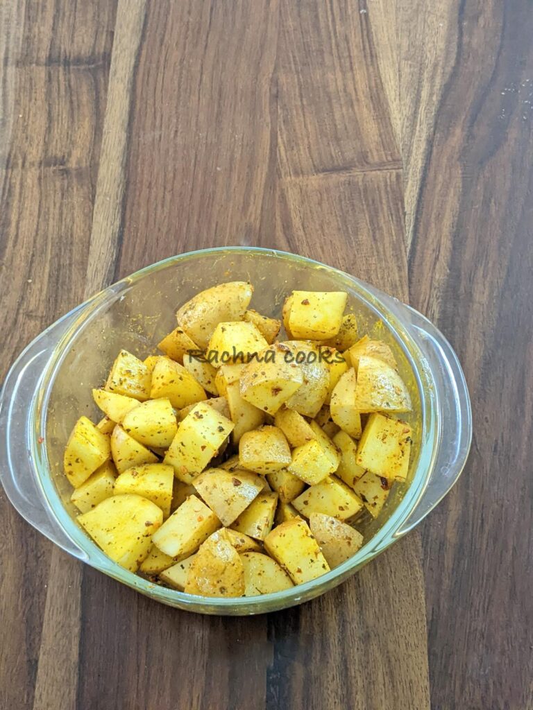 Potato cubes coated with oil and seasonings in a transparent bowl.