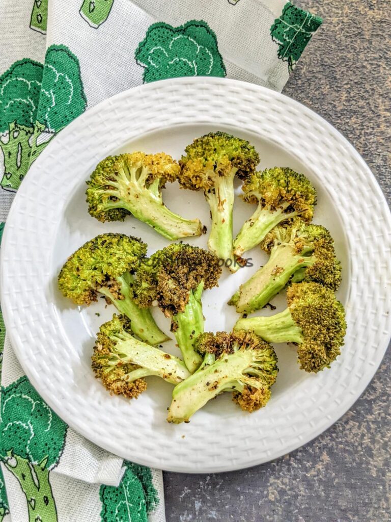 A plate of roasted broccoli florets after air frying against a grey background with a white napkin visible.