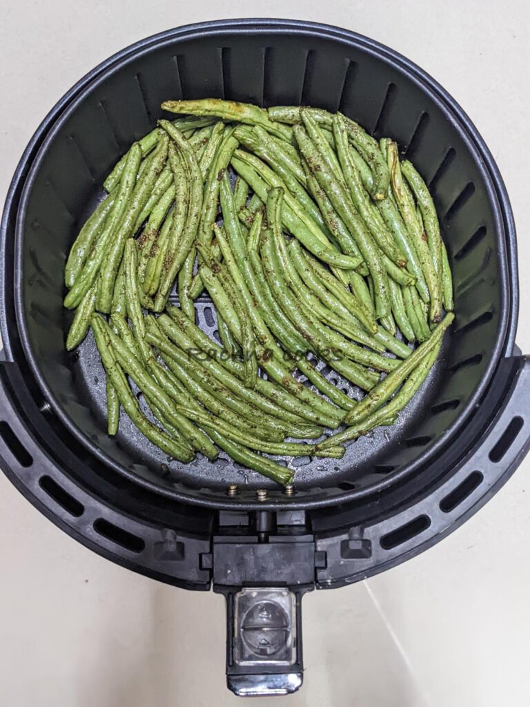 Crispy and cooked green beans in air fryer basket after cooking.