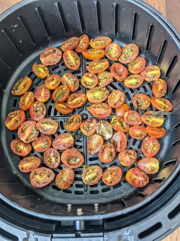 Seasoned cherry tomato halves in air fryer basket ready for air frying.
