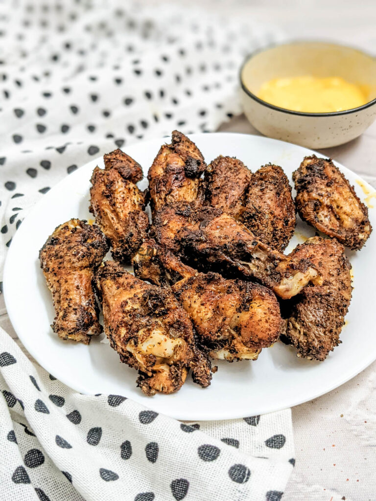 A plate full of air fried chicken wings with a dip on the side.
