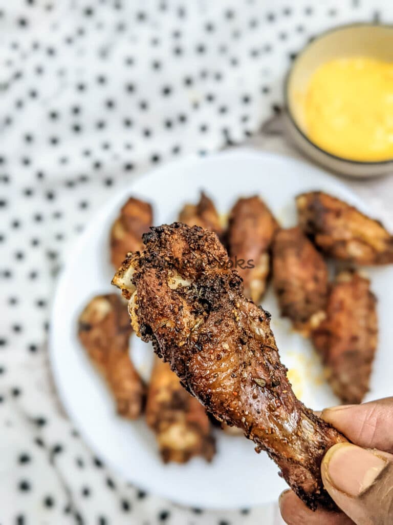 Close up of one air fried chicken wing on a plate full of air fried chicken wings in the background.