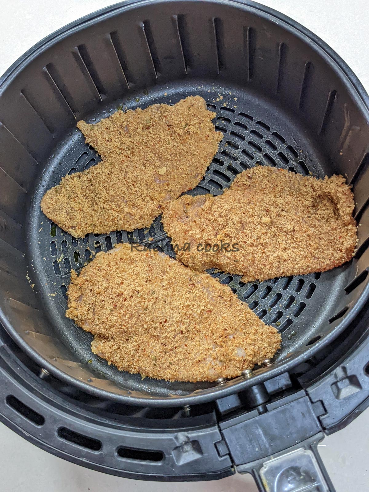 Three breaded chicken breast cutlets ready for air frying in air fryer basket.