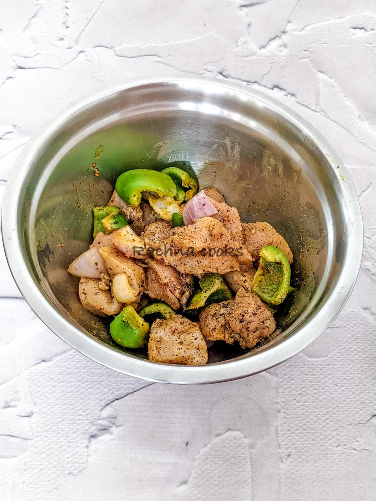 Chicken and veggies marinated in spices and oil in a steel bowl
