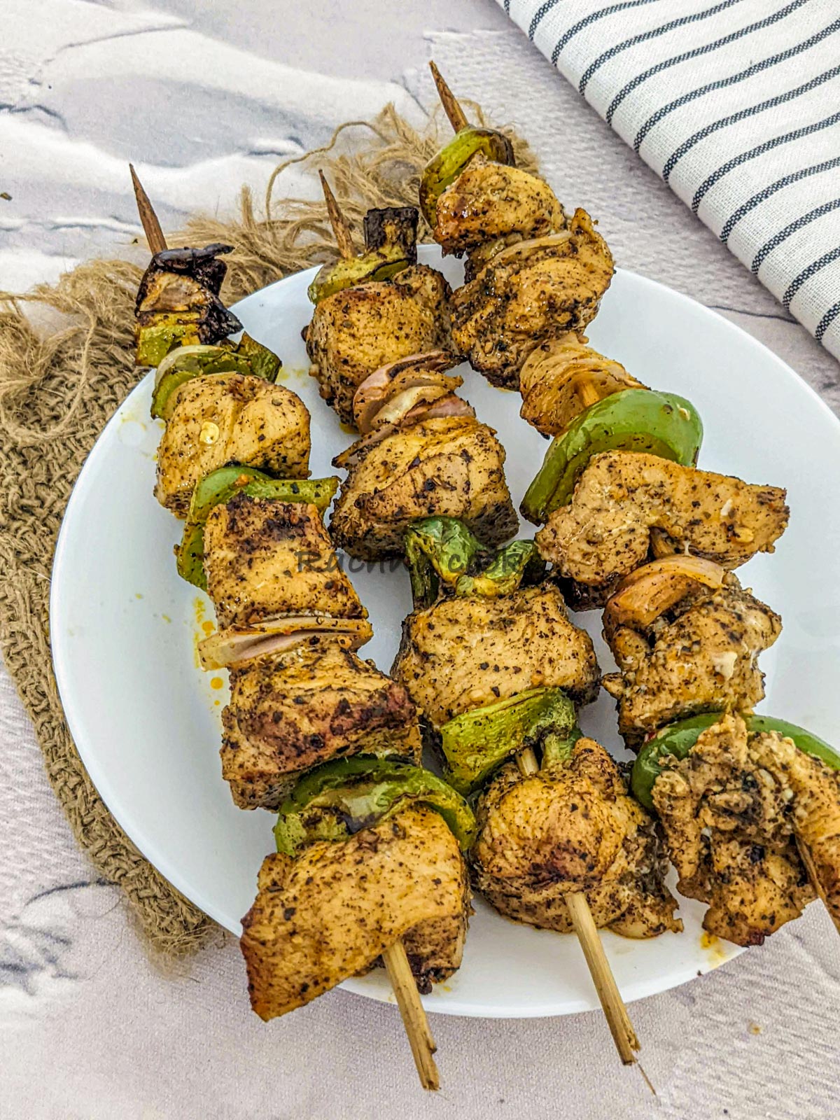 3 skewers of chicken kabobs after air frying served on a white plate.