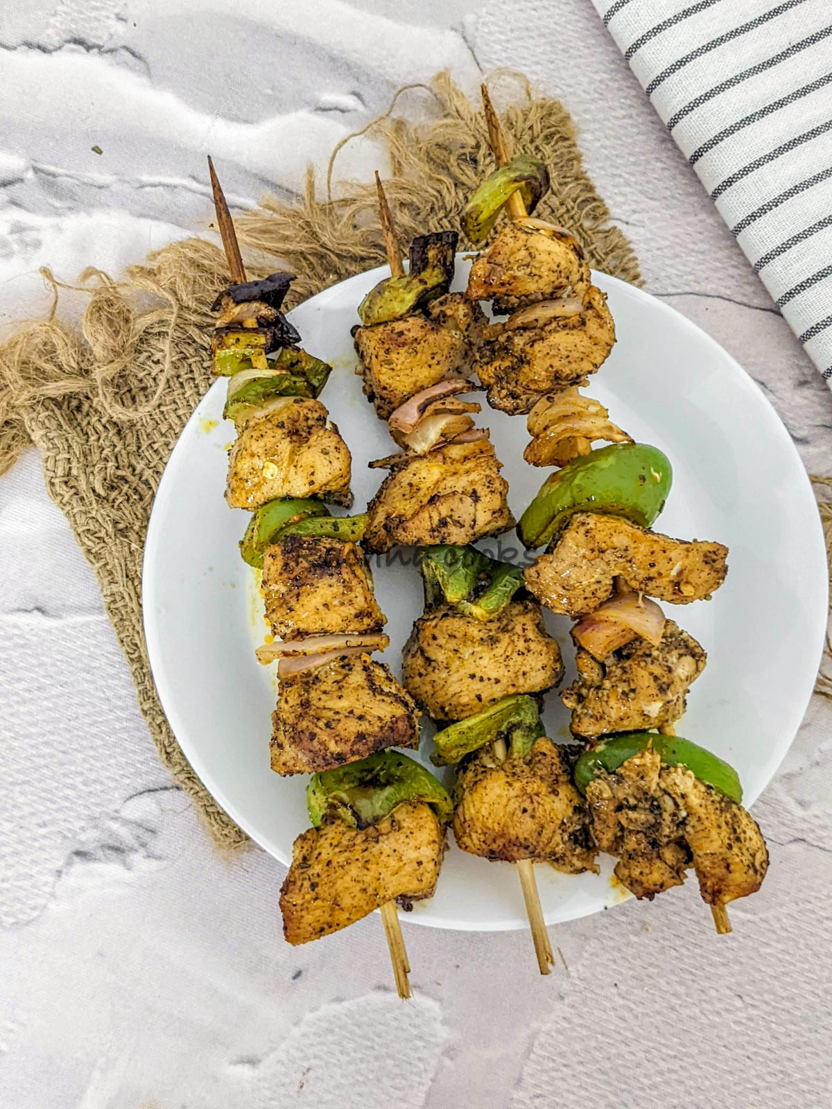 3 skewers of chicken kabob after air frying in a white plate.
