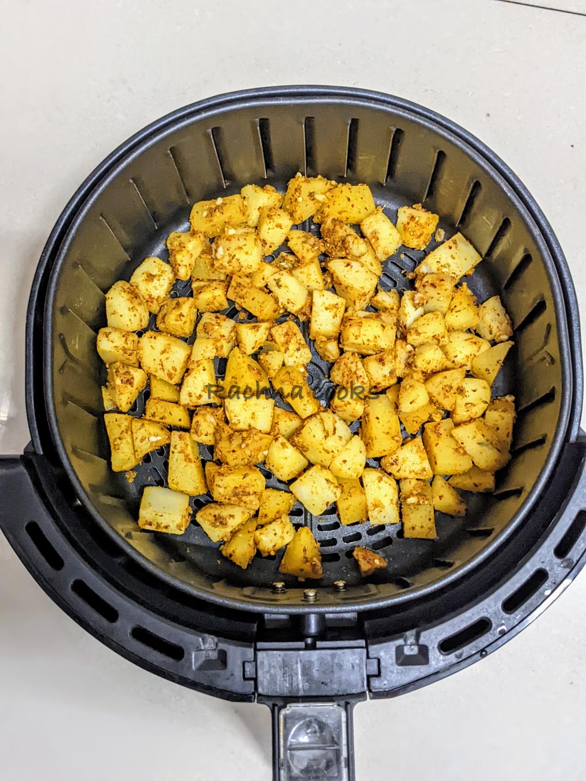 Potato cubes with spices and oil in air fryer basket.