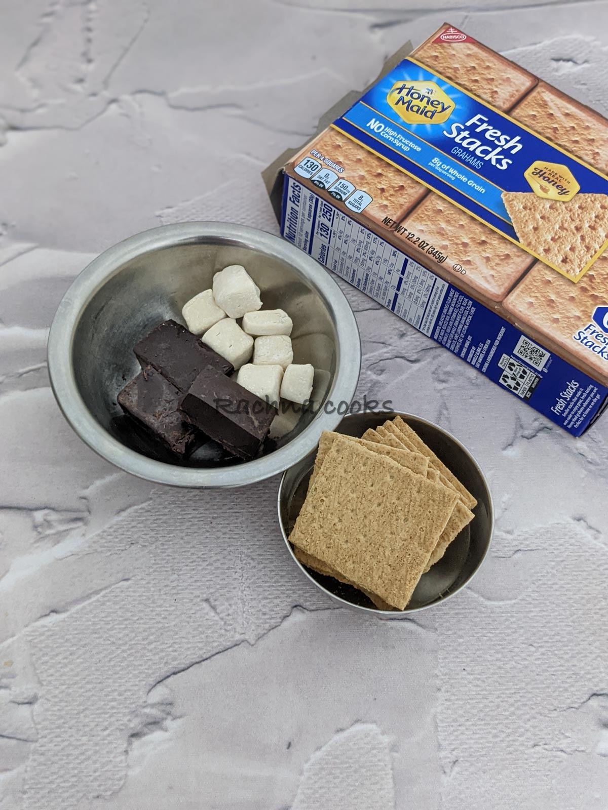 Crackers in a bowl, marshmallows and chocolate bars in another bowl along with a pack of honey maid graham's crackers visible.