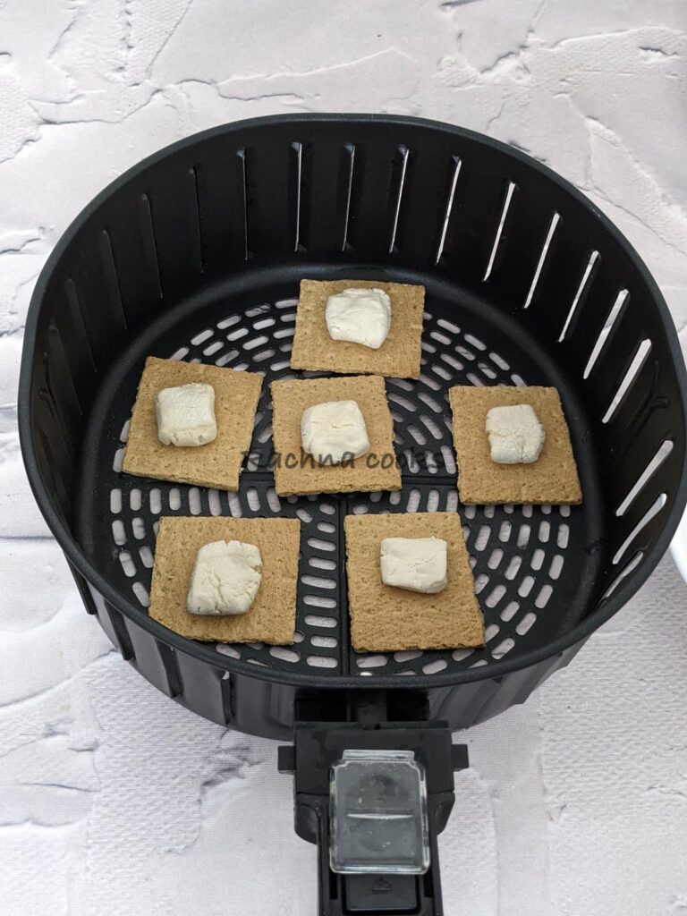 6 crackers with marshmallows on top placed in air fryer basket for air frying.
