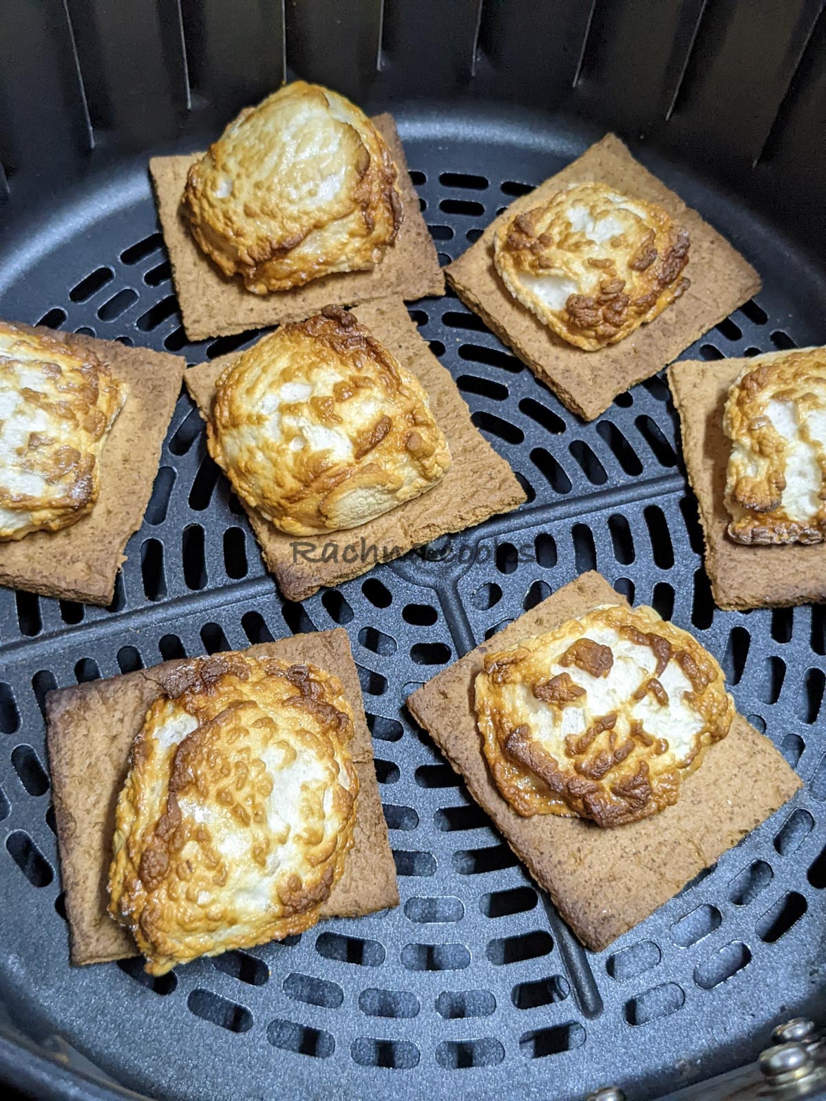Toasted crackers along with roasted marshmallows on top after air frying in air fryer basket.